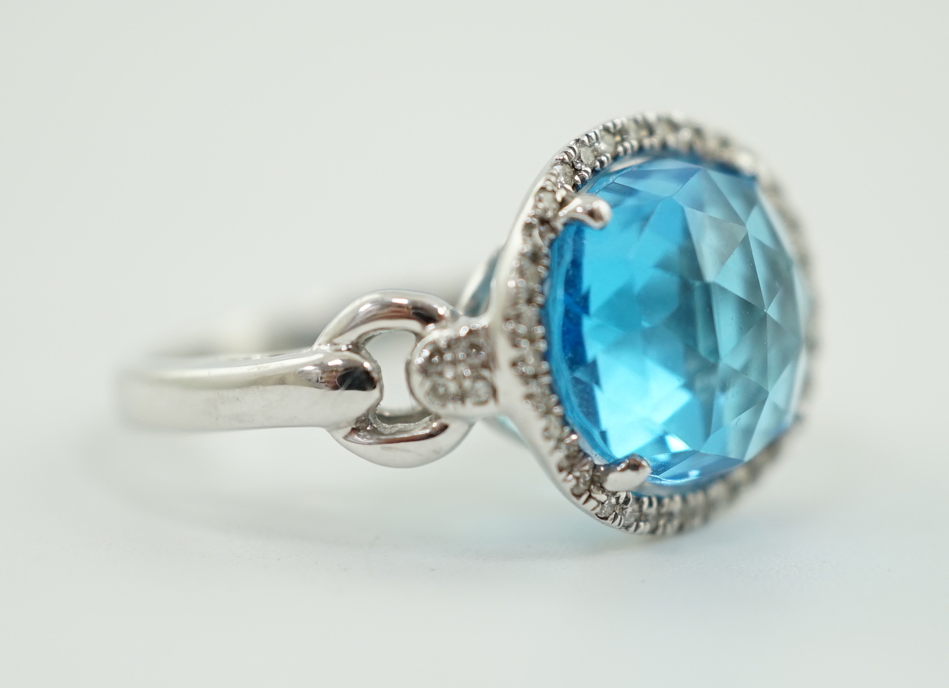 A modern 18ct white gold and facetted oval cut blue topaz set dress ring, with diamond chip set border and shoulders